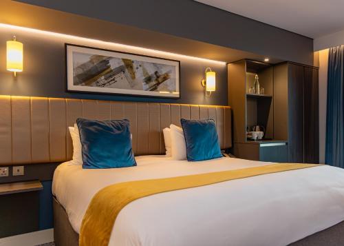 a hotel room with a large bed with blue pillows at Hotel La Tour in Milton Keynes