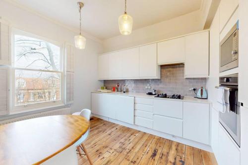 a kitchen with white cabinets and a wooden table at Modern 1BD flat in Clapham Old Town in London