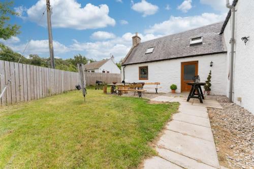 a white cottage with a patio and a fence at Jacobite Lodge by The House of Danu in Kingussie