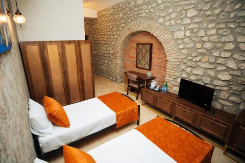 a bedroom with two beds and a tv and a stone wall at Art Hotel by ABAD Guest in Sheki
