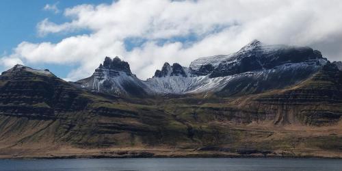 una montaña cubierta de nieve con un cuerpo de agua en Saxa Guesthouse, en Stöðvarfjörður