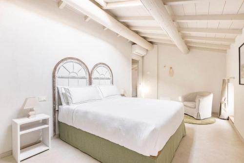 a white bedroom with a large bed and a chair at VerdeOlivo 1876 - Apartments & Pool in Mezzane di Sotto