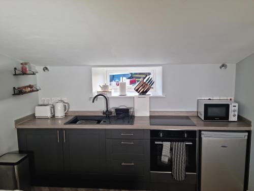 a kitchen with black cabinets and a sink and a microwave at Flamingos Nest Oxford Countryside Apartment Oxford - Bicester Village - Blenheim Palace - WiFi- Free Parking in Oxford