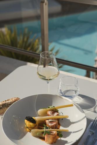 a plate of food and a glass of wine on a table at Hôtel La Plage 5 étoiles La Grande Motte in La Grande-Motte