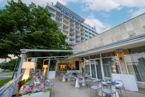 a hotel with tables and chairs in front of a building at Novotel Szeged in Szeged