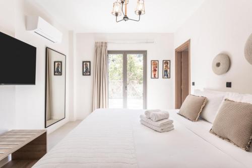 a white bedroom with a large white bed and a tv at Villa Vel Aegina in Vaia