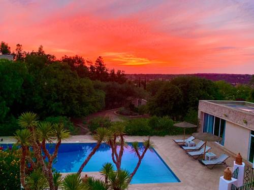 een zonsondergang boven een zwembad met stoelen en bomen bij Le Domaine d'Eden - Villa luxueuse, piscine, spa et personnel in Essaouira