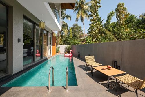 an infinity pool with chairs and a table next to a house at The Banyan Tree Villa B1 by Stay ALYF, Siolim in Siolim