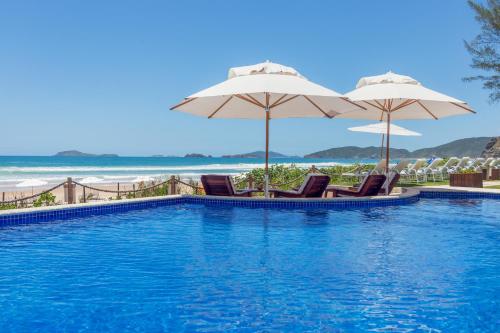 a swimming pool with chairs and umbrellas and the beach at Le Relais La Borie in Búzios