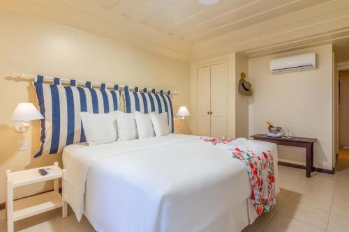 a bedroom with a large white bed with a striped headboard at Le Relais La Borie in Búzios