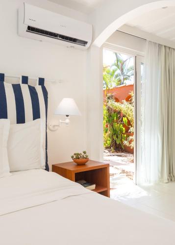 a white bedroom with a bed and a window at Le Relais La Borie in Búzios