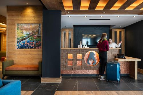 a woman standing at a counter in a restaurant with her luggage at MGM Hôtels & Résidences - Résidence Le Hameau de l'Ours in Manigod