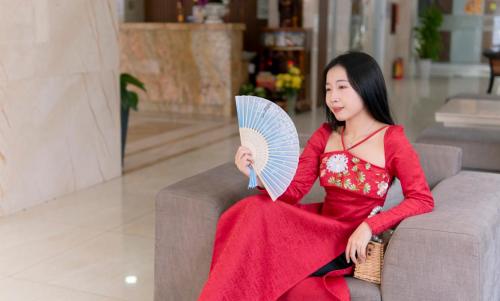 Eine Frau, die auf einer Couch sitzt und einen Ventilator hält. in der Unterkunft Quoc Cuong Center Da Nang Hotel by Haviland in Đà Nẵng