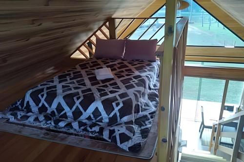 Cama con almohadas moradas en una habitación con ventana en Cabana Pequeno Bosque com deck e vista p/ o rio en São Joaquim