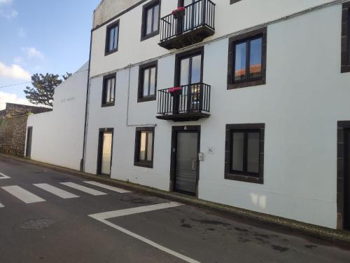 a white building with black windows and balconies on a street at Fenais da Luz House in Fenais da Luz