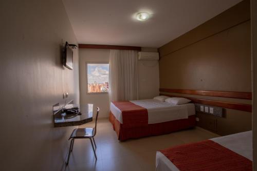 a hotel room with two beds and a desk and a window at Hotel Apollo in Uberlândia