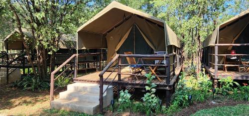 a tent with stairs and a table and trees at Tot Hier Toe in Phalaborwa