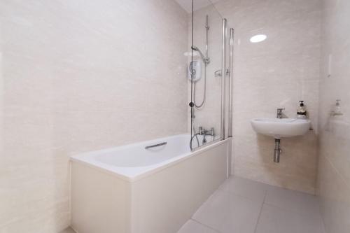 a white bathroom with a shower and a sink at 24 CLIFF APARTMENT-3 BED-GROUND FLOOR-SEA VIEWS in Trearddur