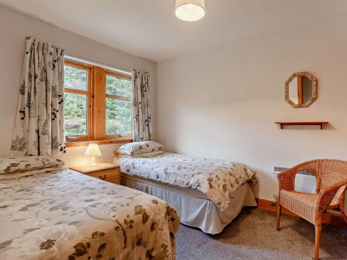 two beds in a room with a window and a chair at 3 Bed in The Cairngorms IN515 in Laggan