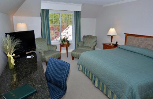 a bedroom with a bed and chairs and a television at Gorges Grant Hotel in Ogunquit