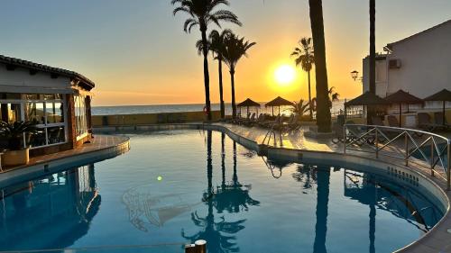 einen Pool mit Palmen und dem Meer bei Sonnenuntergang in der Unterkunft Appartement Dona Lola Bord de mer in Mijas Costa