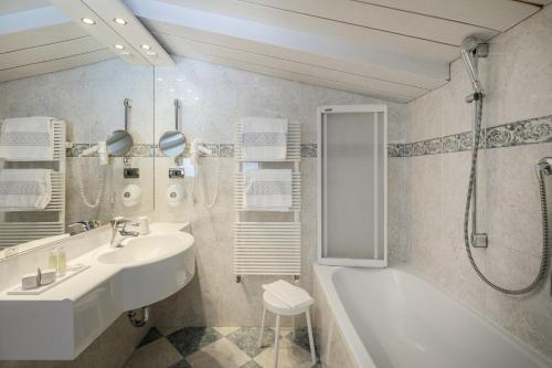 ein weißes Bad mit einem Waschbecken und einer Dusche in der Unterkunft Piccolo Hotel in Wolkenstein in Gröden