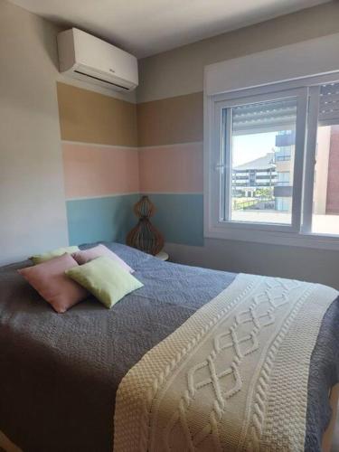 um quarto com uma cama com duas almofadas e uma janela em Apartamento Capão da Canoa com garagem em Capão da Canoa
