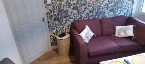 un sofá púrpura en una sala de estar con papel pintado con motivos florales en The Woodlands apartments 1, en Londres