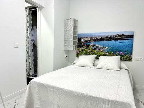 a bedroom with a white bed with a painting on the wall at Alcalá Retreat: Ocean View & Modern Comfort in Alcalá