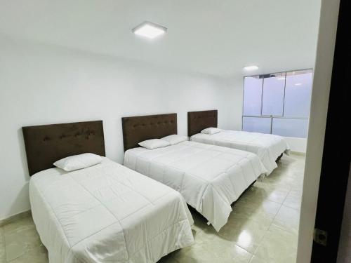two beds with white sheets in a room with a window at Departamento Los viñedos in Ica
