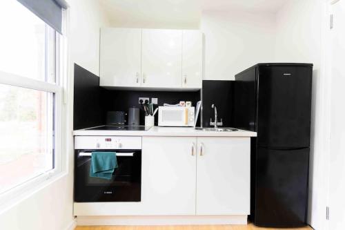 バーミンガムにあるExclusive Studio Retreatのキッチン(白いキャビネット、黒い冷蔵庫付)