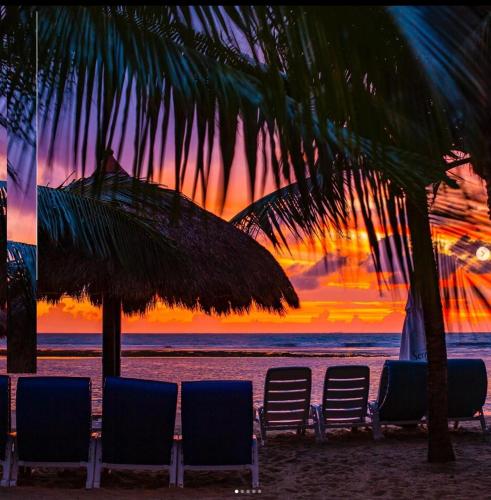 a group of chairs and umbrellas on a beach with a sunset at Serrambi Resort in Porto De Galinhas