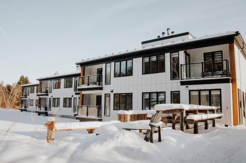 un bâtiment recouvert de neige avec des bancs et des tables dans l'établissement Suite 104- Destination Mont-Orford, à Magog