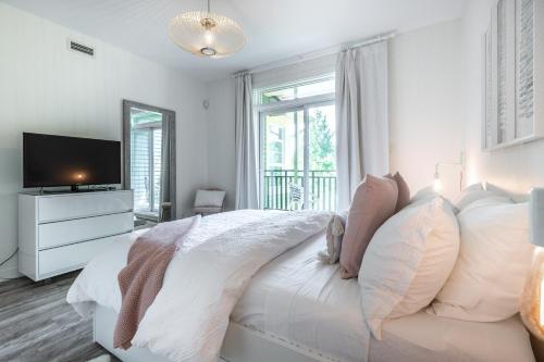 a white bedroom with a bed and a television at Les Eaux 227-3 by Tremblant Prestige in Mont-Tremblant