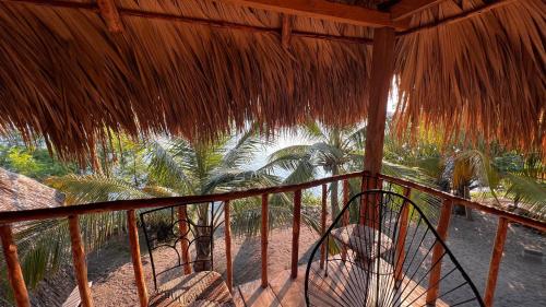 a porch with a straw roof with palm trees at Cabañas Casa de Agua in Boca del cielo
