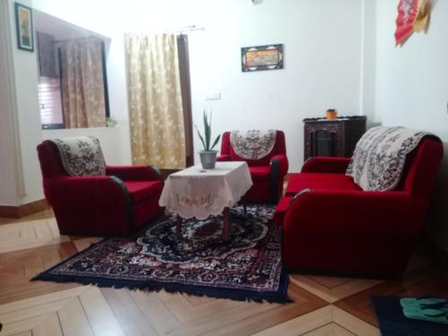 una sala de estar con 2 sillas rojas y una mesa. en Areca Holiday Apartment, en Siliguri