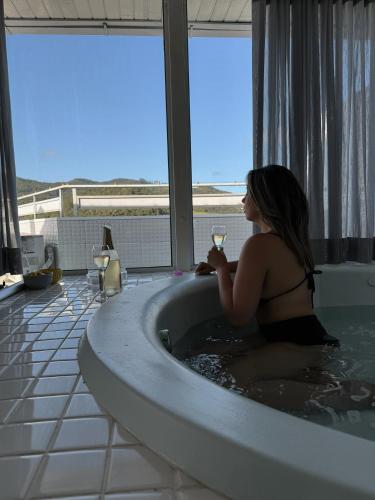 uma mulher numa banheira com um copo de vinho em Duplex Ametista em Gravatal