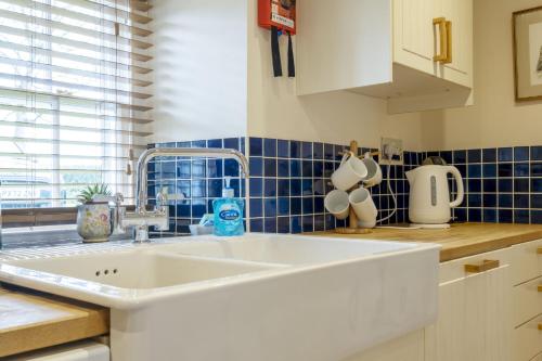uma cozinha com um lavatório branco e azulejos azuis em White Lodge Haughton Castle em Hexham