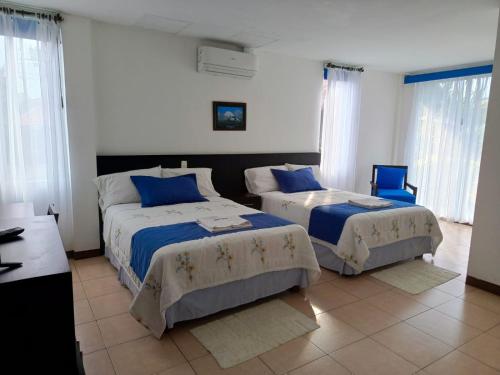 a bedroom with two beds and two blue chairs at Hotel Yurak in Archidona