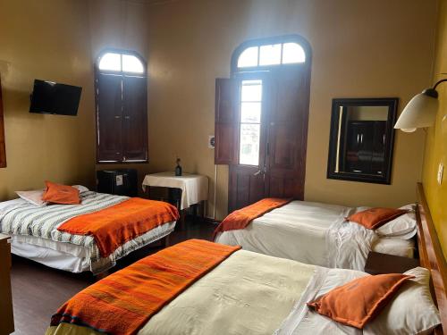 Habitación con 3 camas, TV y ventanas. en La Casona de Palacio Viejo, en Arequipa