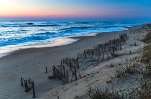 a fence on the beach at sunset at Holiday Inn Express Nags Head Oceanfront by IHG in Nags Head