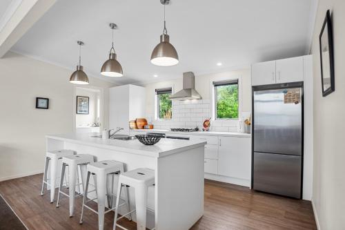 a kitchen with white cabinets and a large island with bar stools at Relax on Dillon - Waihi Beach Holiday Home in Waihi Beach