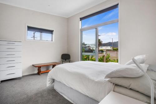 a white bedroom with a bed and a window at Relax on Dillon - Waihi Beach Holiday Home in Waihi Beach