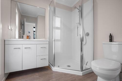 a white bathroom with a shower and a toilet at Relax on Dillon - Waihi Beach Holiday Home in Waihi Beach