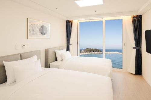 two white beds in a room with a large window at Surf Resort JD Yangyang in Yangyang