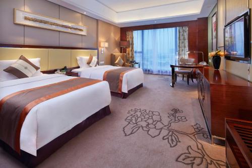 a hotel room with two beds and a desk at Guangzhou ChangFeng Gloria Plaza Hotel in Zengcheng