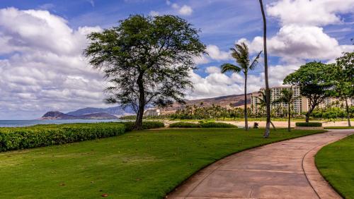 a path through a park with palm trees and the ocean at Ko Olina Beach Villas O401 in Kapolei