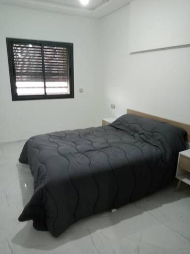 Cama negra en habitación blanca con ventana en Family Vacation Apartment- VacayX- Temara, en Temara