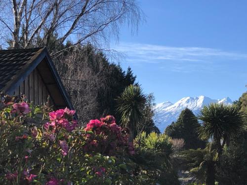 a house with flowers and mountains in the background at Unique and Charming Garden Cottage/Campervan in Rangataua