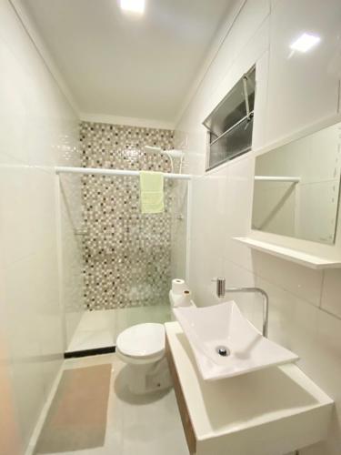 a white bathroom with a toilet and a sink at Casa praia 99 in Serra